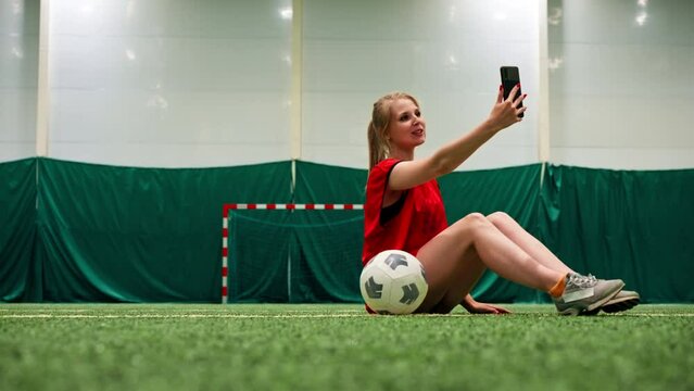 smiling young soccer girl blogger taking photo on phone taking selfie with ball on soccer field
