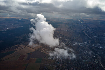 Aerial view from airplane window at high altitude of distant city covered with puffy cumulus clouds...