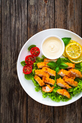 Seared breaded chicken nuggets with mayonnaise and fresh vegetables on wooden table
