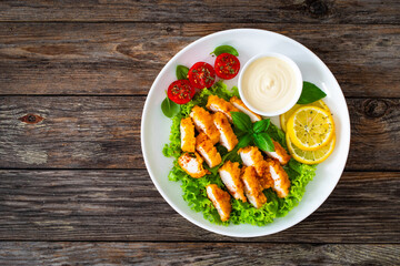 Seared breaded chicken nuggets with mayonnaise and fresh vegetables on wooden table
