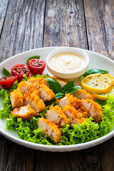 Seared breaded chicken nuggets with mayonnaise and fresh vegetables on wooden table

