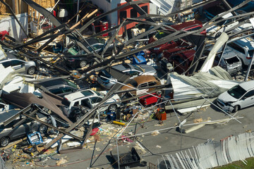 Car dealership building destroyed by hurricane with damaged cars under ruins in Florida. Natural...