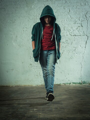 Boy walking straight towards the camera with hoodie untied and hood up. Urban and industrial...