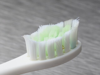Old white toothbrush with white and green bristles on a metal background