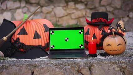 A laptop with a green screen with dots for tracking movement against the background of Halloween props, bats, pumpkins, skulls, spiders, brooms, burning candles. The concept of application advertising