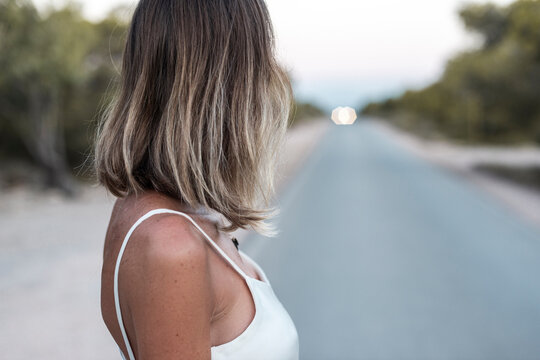 Unrecognizable woman wearing white dress on abandoned road at dusk
