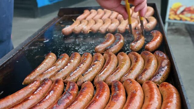 Close-up of sausages on the grill, male hand frying pork bratwurst.