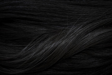 Brunette or black hair. Female long dark hair in black. Beautifully laid curls. Closeup texture in a dark key. Hairdressing, hair care and coloring. Shading gray hair. Background with copy space.