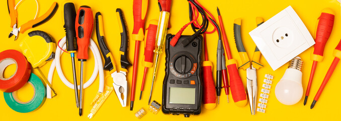 Electrician tools on yellow background.Multimeter,construction tape,electrical tape, screwdrivers,pliers,an automatic insulation stripper, socket and LED lamp.Flatley.electrician concept.