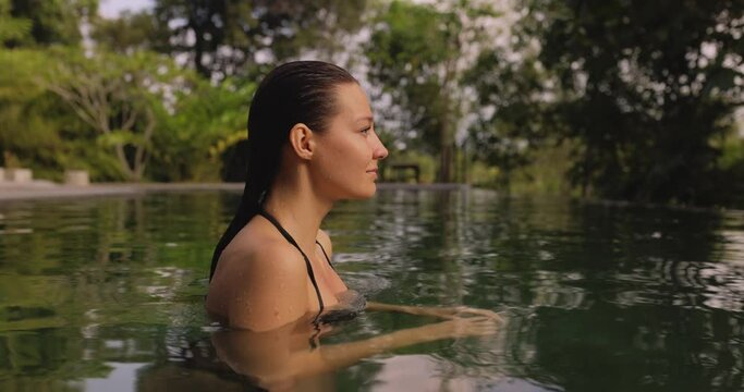 Amazing bathing spa woman pops up from a luxurious infinity pool, wearing a fashionable bikini and flaunting her perfect tanned buttocks. Cinematic slow-motion video in 4k