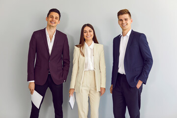 Team of happy young business people standing in the office. Group of two men and one woman wearing...