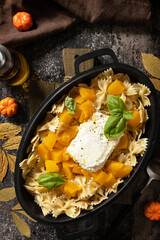 Feta pasta recipe made of pumpkins, feta cheese, garlic and herbs on dark stone background. Fetapasta. Baked feta pasta, or Tiktok pasta. View from above.