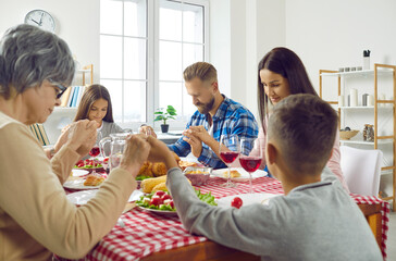 Family praying before meal. Adults and little children celebrating festive event like Thanksgiving Day, sitting all together around dinner table, holding hands, saying prayer, thanking God for food