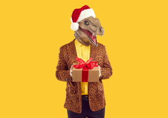 Eccentric man in dinosaur head mask with gift box. Portrait of weird guy wearing Santa Claus hat, leopard jacket and yellow shirt holding cardboard box with red bow. Christmas and New Year celebration