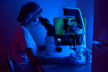 Scientist embryologist in mask works with biomaterial under microscope
