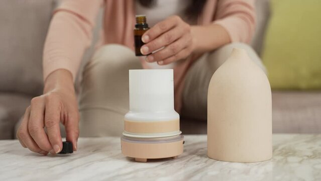slow motion with closeup shot hands of asian female putting essential oil drops into diffuser on table. healthy lifestyle and aromatherapy at home concept