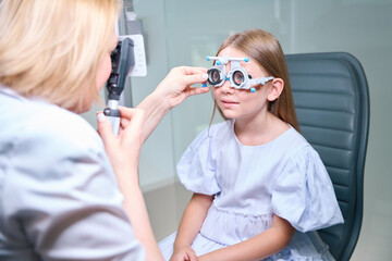 Experienced female optometrist carrying out dynamic retinoscopy on child - obrazy, fototapety, plakaty