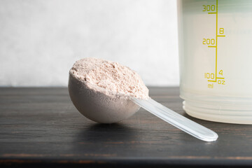 Whey chocolate protein powder in a plastic measuring spoon on a dark wooden board and white background