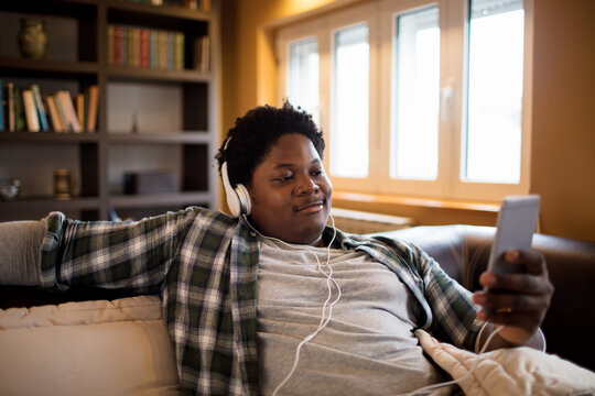 Young African American Man Listening To Music On His Smartphone On The Couch In The Living Room At Home