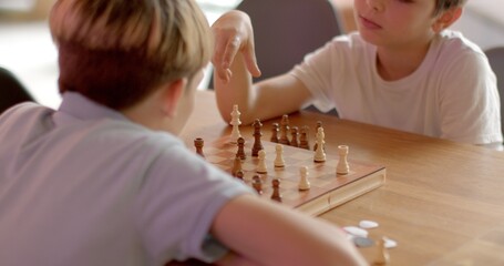 Two children playing chess in cafe, friendly interaction. Kids mentally stimulating indoor...