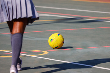 african american girl with a plated school skirt on the sports field chasing a yellow ball