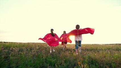 Little children wearing red capes play superheroes running across field