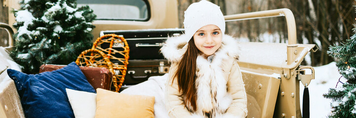 cute beautiful little Armenian girl in winter coat and knitted hat sit near beige retro pickup...