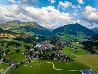 Aerial shot of beautiful alpine landscape with town, hills and deep valleys. Picturesque golden hour in mountains. Gstaad, Switzerland