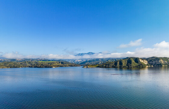 Aerial panoramic shot of lake water surface and mountains shrouded in clouds in distance. Amazing landscape photo. Cachuma Lake, California, USA