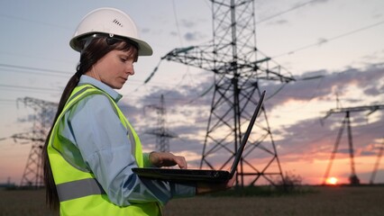 Fototapeta na wymiar Concentrated employee with helmet works on laptop near power transmission lines