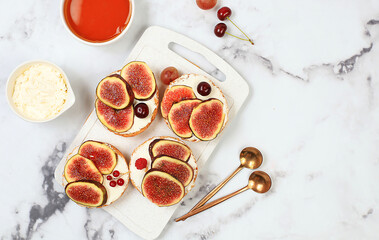 Ricotta,figs and bruschetta with honey on gray marble.Fresh sandwiches and toast with cream cheese,sliced figs,honey and cherries.Healthy breakfast with ingredients,lunch or dessert,diet food concept