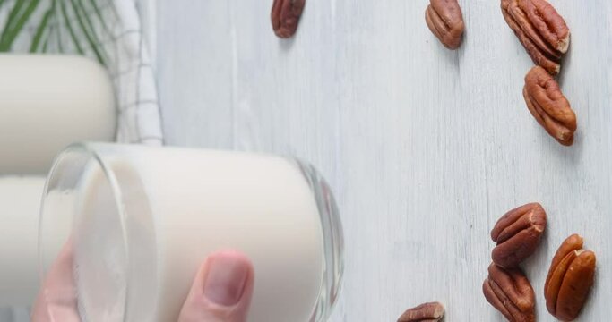 Hand taking a glass with vegan milk, Close-up video of non-dairy drink made of pecan nuts placed on white table, 4k video, slow motion footage 