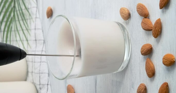 Making milk foam from vegan almond drink with automatic rotating milk frother, speed up video clip, using milk foam maker to prepare foam for coffee drinks, 4k footage, vertical clip for social media