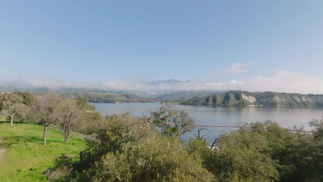 Forwards fly above trees. Revealing lake with cliffs on opposite bank and mountains in background. Cachuma Lake, California, USA