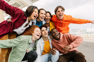 Excited young group of multiracial people having fun together outdoors. Millennial friends enjoying travel vacation in city street. Friendship concept.