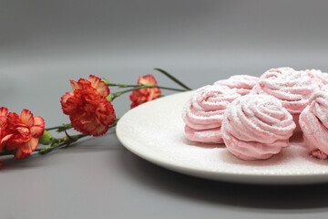 Delicate handmade marshmallows on a white plate with flowers on a gray background.