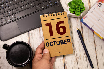 Wooden calendar with date October 16 and alarm clock on table against brick wall background.