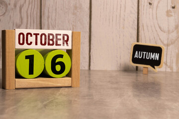 Wooden calendar with date October 16 and alarm clock on table against brick wall background.