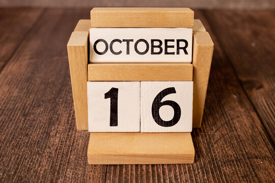 Wooden calendar with date October 16 and alarm clock on table against brick wall background.