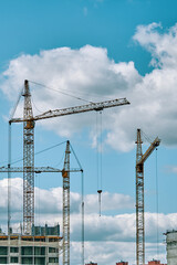 Industrial building cranes on background of cloudy sky. Hoisting cranes and multi-storey buildings of new city districts. Construction site background with copy space.