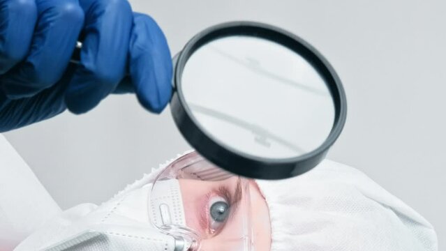 Vertical video. Virology research. Medical examination. Woman doctor laboratory specialist in protective suit equipment with loupe isolated on grey background.