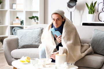 Ill young man with hot water bottle eating soup at home