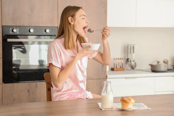 Young woman eating breakfast cereal with milk in kitchen - obrazy, fototapety, plakaty
