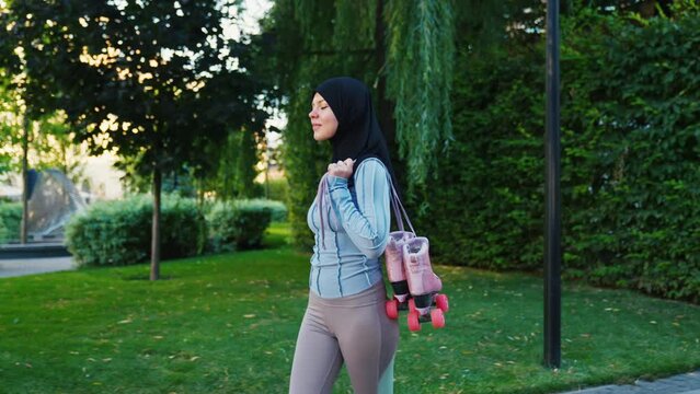 Stable shot of young muslim woman in black hijab carrying quad roller skates and riding in city