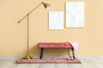 Paintings, standard lamp and pink bench near beige wall