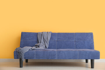 Stylish blue sofa with blanket near orange wall