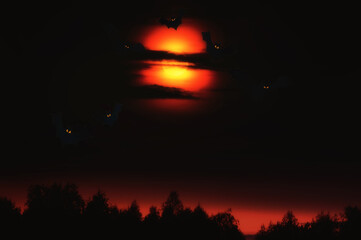 Dark gloomy night photo of a full red moon in the clouds and toy bats. Halloween mood