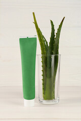 Tube of toothpaste and fresh aloe vera leaves on white wooden table