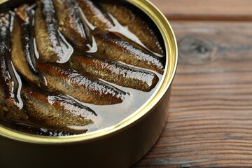 Open tin can of sprats on wooden table, closeup