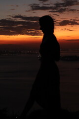 Silhueta de uma linda mulher no pôr do sol alaranjado com a cidade ao fundo